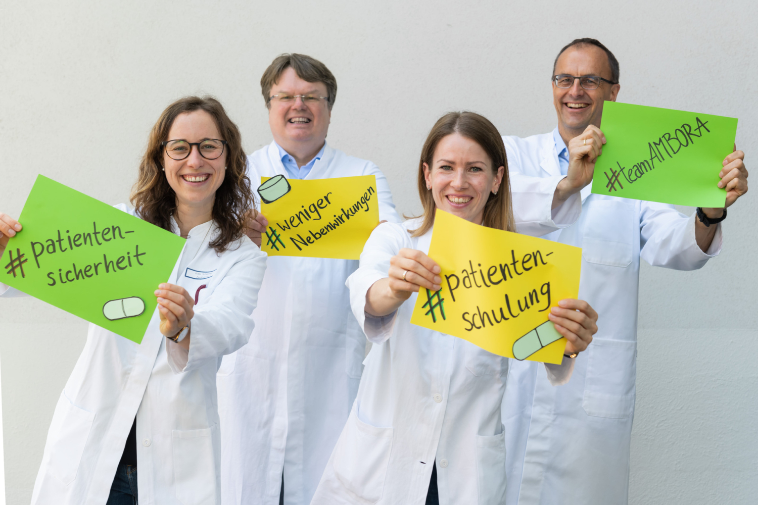 Mitglieder des AMBORA-Teams halten bunte Zettel in den Händen. Darauf sind Hashtags patientensicherheit, patientenschulung, weniger nebenwirkungen und teamAMBORA zu lesen