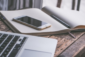 Digitales Arbeitssetup mit Laptop, Smartphone und Notizbuch – weiter zu News & FAQ zur oralen Tumortherapie