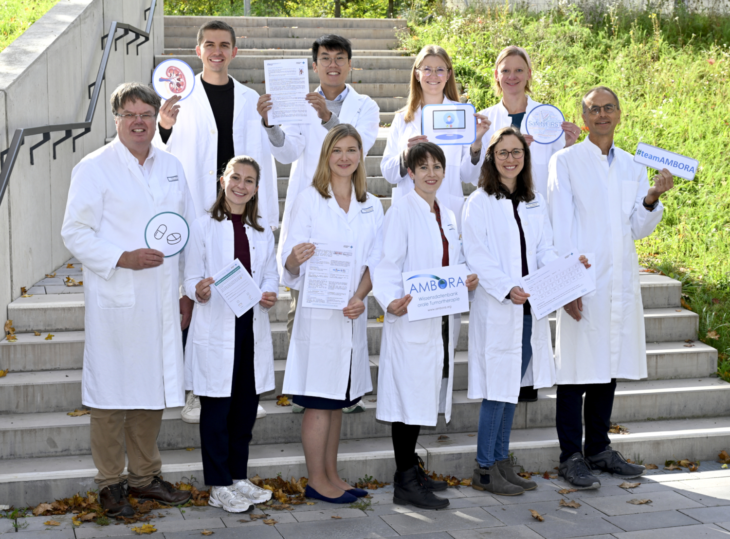 Ein Gruppenfoto der AMBORA Team-Mitglieder zeigt in der hinteren Reihe Michael Sponfeldner, Sam Huynh, Maike Simon und Julia Schwanfelder und in der vorderen Reihen Projektleiter Prof. Dr. Frank Dörje, Phyllis Lensker, Sophia Reinhold, Pauline Dürr, Dr. Katja Gessner und Projektleiter Prof. Dr. Martin F. Fromm. Alle Teammitglieder halten Bilder ihrer Schwerpunkt-Projekte in der Hand.